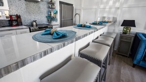 Een moderne keuken met een centraal eiland, barstoelen, een koelkast en een koffiezetapparaat.