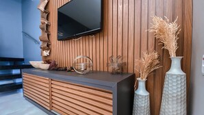A modern reception area with a wooden panel wall, a flat-screen TV mounted above a dark counter, and decorative vases with dried plants. - House with 2 bedrooms in the Monte das Oliveiras Condominium in Arraial D'Ajuda (Arraial d'Ajuda)