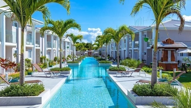 A resort with a central swimming pool flanked by palm trees and lounge chairs, surrounded by white buildings with balconies. - House with 2 bedrooms in the Monte das Oliveiras Condominium in Arraial D'Ajuda (Arraial d'Ajuda)