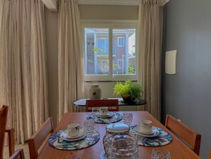 Un coin repas avec une table dressée pour quatre personnes, une plante en pot et une fenêtre donnant sur des immeubles.