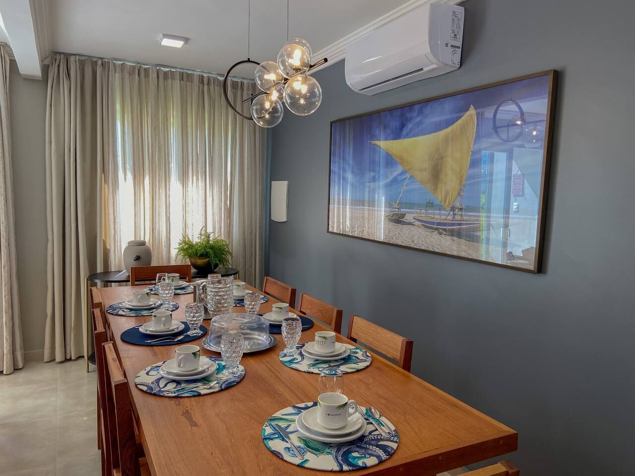 A dining area with a wooden table set for a meal, a painting on the wall, and an air conditioning unit above the table.