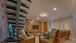 A modern living room with a sofa set, a small table with decorative items, a flat-screen TV mounted on the wall, and a wooden accent wall. - House with 2 bedrooms in the Monte das Oliveiras Condominium in Arraial D'Ajuda (Arraial d'Ajuda)