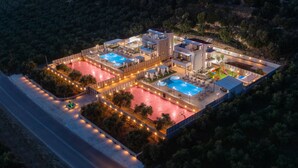 Vue aérienne d’un complexe hôtelier moderne doté de plusieurs piscines, d’un grand espace couvert et d’un périmètre bien éclairé.