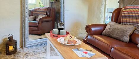 A cozy living room with a brown leather sofa, a wooden coffee table with a plate of food, a large mirror, and a rustic lamp.