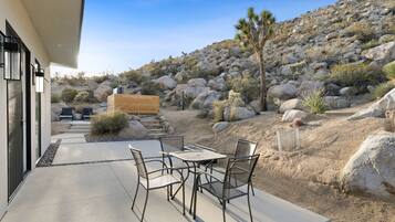 Une terrasse extérieure avec une table et des chaises, entourée de rochers et de plantes désertiques.