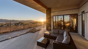 Un espacio exterior moderno con sofá, mesa de centro, puertas de cristal amplias y vistas al paisaje.