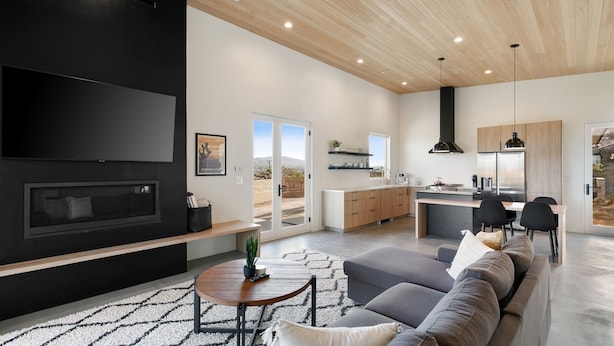 Una sala de estar moderna con un televisor grande, una chimenea y un sofá. Hay una zona de cocina con una mesa de comedor y sillas.