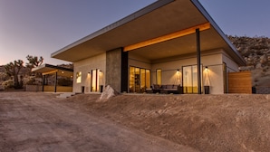 Una casa moderna con un amplio alero, un patio con asientos y vistas del paisaje circundante.