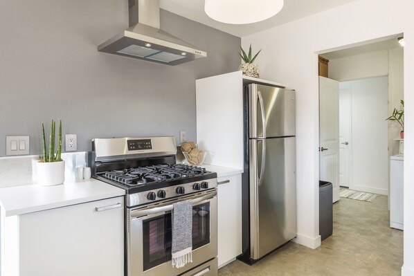 Una cocina moderna con estufa, horno y refrigerador de acero inoxidable, gabinetes blancos y una planta en la encimera.