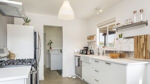 A modern kitchen with white cabinetry, a stainless steel stove, and a wooden dining table. - Live Centered W/ Hot Tub, Fire Pit In Joshua Tree 2 Bedroom Home by RedAwning (Joshua Tree)