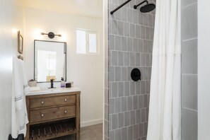 A bathroom with a wooden vanity, a mirror, a shower with a rain showerhead, and a tiled shower wall.
