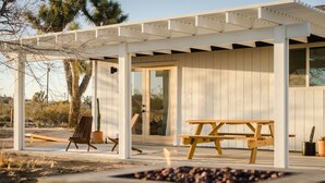 A covered outdoor area with a wooden bench and a fire pit. - Mojave Mesa - Desert Views & Desert Style 1 Bedroom Home by RedAwning (Yucca Valley)