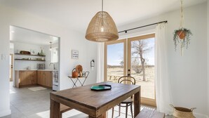 A modern kitchen with wooden cabinets, a dining area with a wooden table, and a large window with a view of the outdoors. - Mojave Mesa - Desert Views & Desert Style 1 Bedroom Home by RedAwning (Yucca Valley)