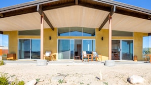 A modern building with a covered patio, large sliding glass doors, and outdoor seating. - Las Alas Del Sol- A Desert Architectural Gem 2 Bedroom Home by RedAwning (Joshua Tree)