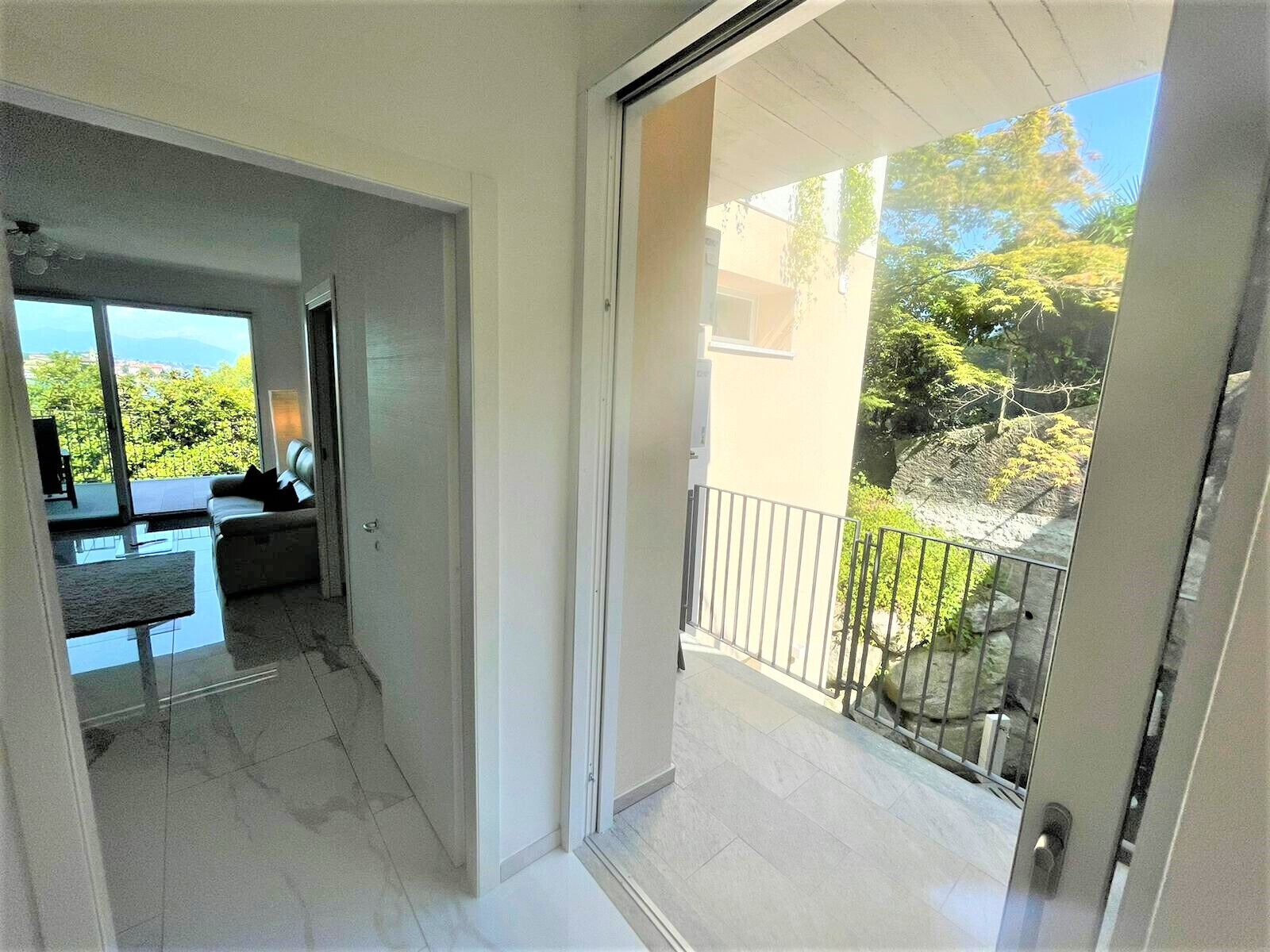 Een modern interieur met balkon, een bank en uitzicht op groen.