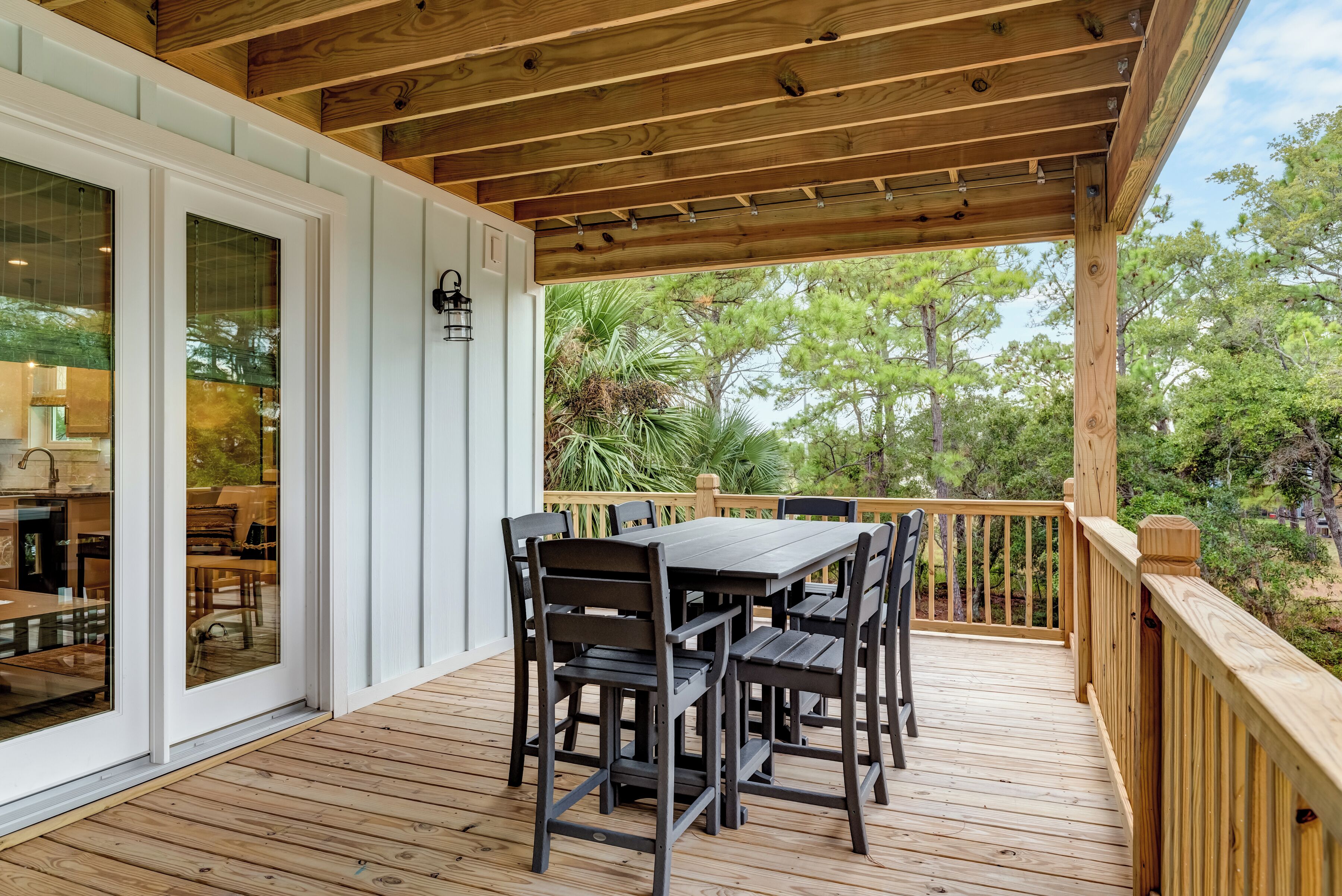 Une terrasse extérieure couverte, avec une table et des chaises en bois, une balustrade en bois et une vue sur les arbres.