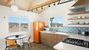 Une cuisine donnant sur un paysage désertique, avec un four moderne et un réfrigérateur orange d’époque.
