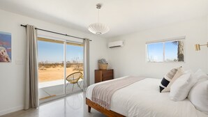 Une chambre avec un grand lit, une table de chevet en bois, une chaise et une vue sur le désert, visible à travers une porte coulissante.