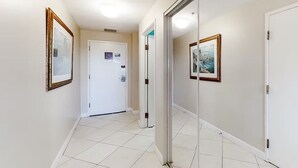 A hallway with a white door, framed pictures on the walls, and a tiled floor. - Tops'l 1008a Chalet by RedAwning (Miramar Beach)