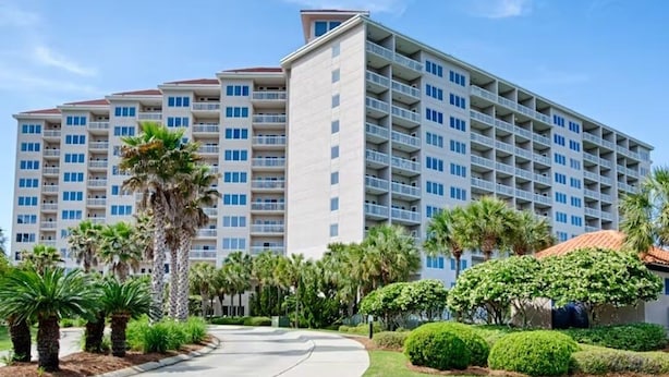 A multi-story hotel with a modern design, featuring balconies on each floor and a well-maintained garden area with palm trees and shrubs. - Tops'l 1008a Chalet by RedAwning (Miramar Beach)