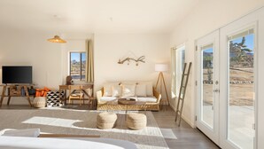 A spacious room with a large bed, a sofa, a TV, and a dining area. - Rancho Nopales Jt - Pool, Hot Tub, Hammocks, Fast Wifi + Views! 4 Bedroom Home by RedAwning (Joshua Tree)