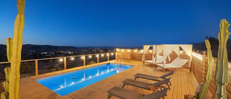 Um deck de madeira com piscina, cadeiras de sol e cactos.