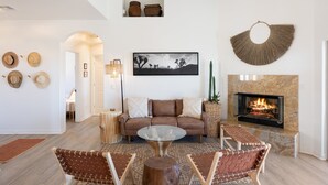 A living room with a sofa, two armchairs, a coffee table, a fireplace, and a wall-mounted picture. - Rancho Nopales Jt - Pool, Hot Tub, Hammocks, Fast Wifi + Views! 4 Bedroom Home by RedAwning (Joshua Tree)