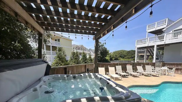A hot tub under a pergola with a pool and lounge chairs in the background. - OBXLanai - 5 houses from Private Duck Beach + Private Pool at House! (Kitty Hawk)
