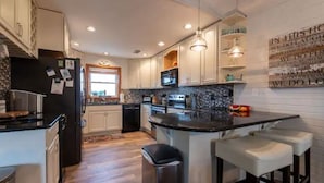 A modern kitchen with white cabinets, a black refrigerator, a microwave, and a granite countertop. - OBXLanai - 5 houses from Private Duck Beach + Private Pool at House! (Kitty Hawk)