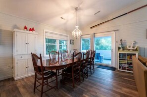 A dining area with a wooden table and chairs, a chandelier, and a view through the glass door.
