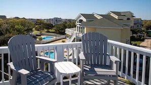 A balcony with Adirondack chairs overlooking a swimming pool and a residential area. - OBXLanai - 5 houses from Private Duck Beach + Private Pool at House! (Kitty Hawk)