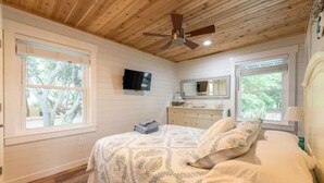 A bedroom with a wooden ceiling, a bed with patterned bedding, a dresser, a mirror, and a television on the wall. - OBXLanai - 5 houses from Private Duck Beach + Private Pool at House! (Kitty Hawk)
