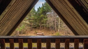 Una estructura de madera triangular con un banco y una mesa de picnic en un área boscosa.