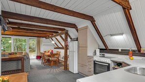 Una cocina acogedora en el ático, con vigas de madera, un comedor con mesa y sillas, y vistas al exterior a través de amplios ventanales.