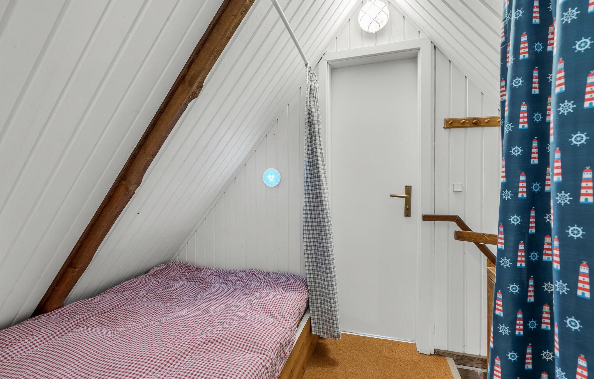 A small, single-bed room with a sloped ceiling, a wooden door, and a light fixture on the wall.