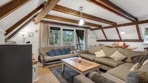 Una sala de estar estilo loft acogedora, con vigas de madera a la vista, un ventanal con vistas a árboles, una chimenea y un comedor con una tetera roja.