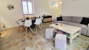 A modern living room with a grey sofa, a white coffee table, and a dining area with white chairs and a kitchen in the background. - Trémélois - TREMEL - Gîte (TREMEL)