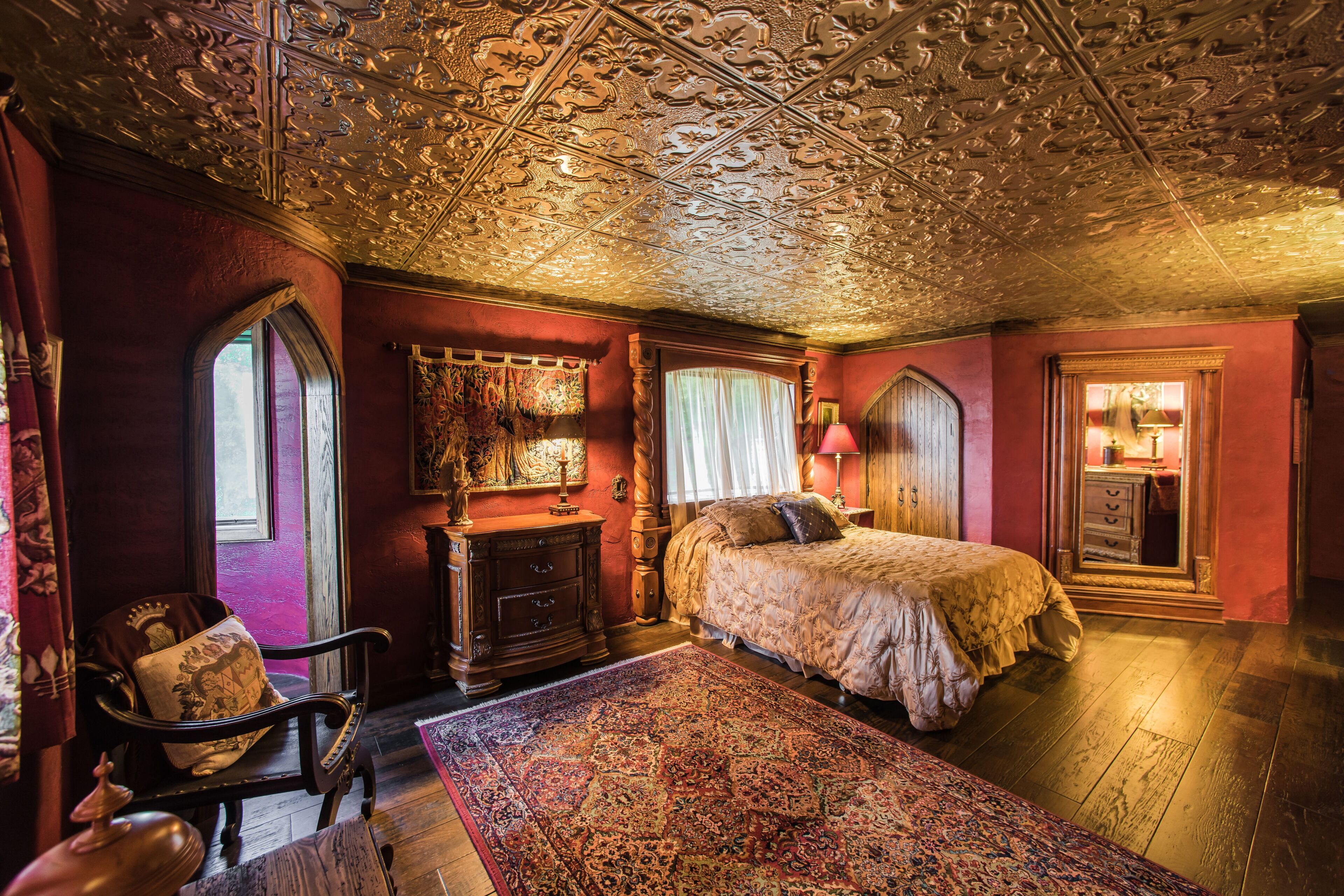 Een kamer met een groot, versierd plafond, een bed, een houten dressoir en een stoel.