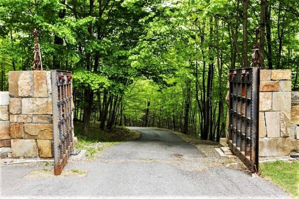 A paved pathway flanked by stone walls and metal gates, leading through a forested area.