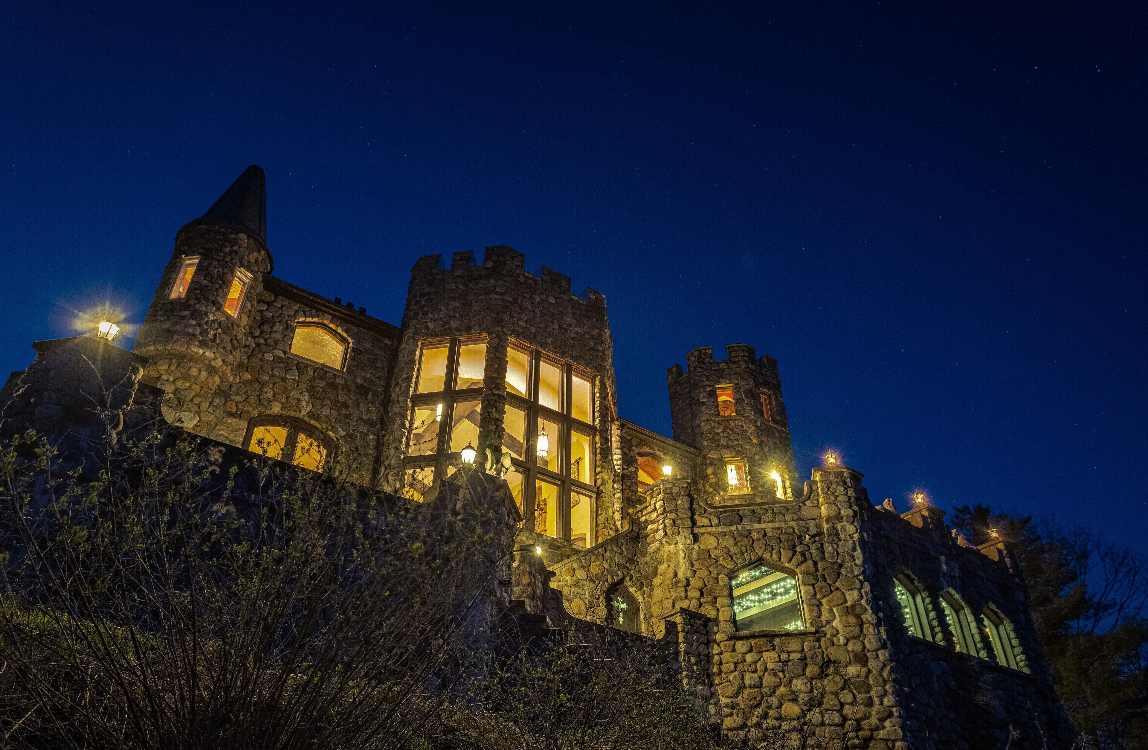 A stone castle-like building with multiple windows and a tower at night.