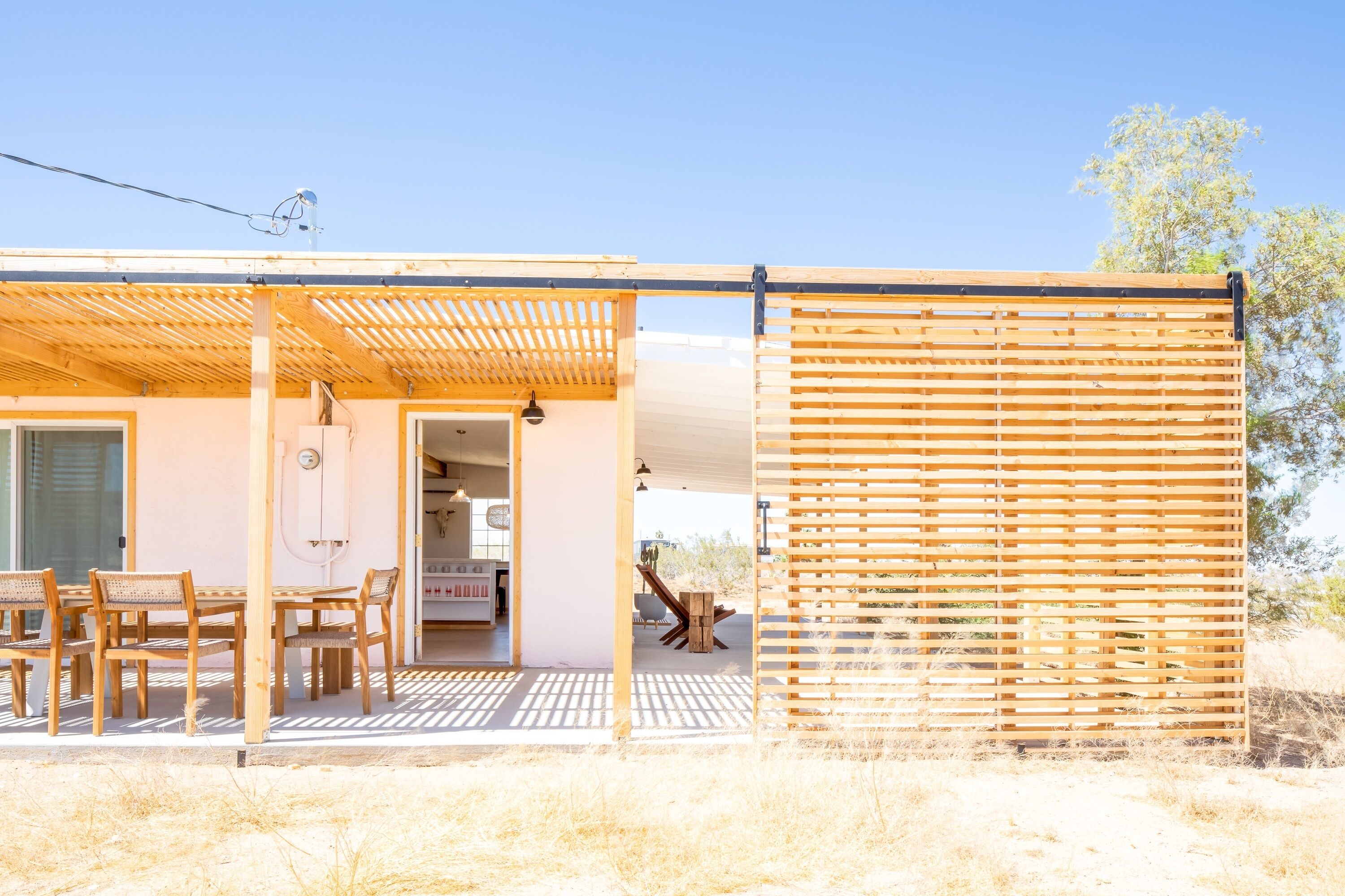 Een modern huis met een overdekte patio, een eethoek met houten meubels en uitzicht op het omliggende landschap.