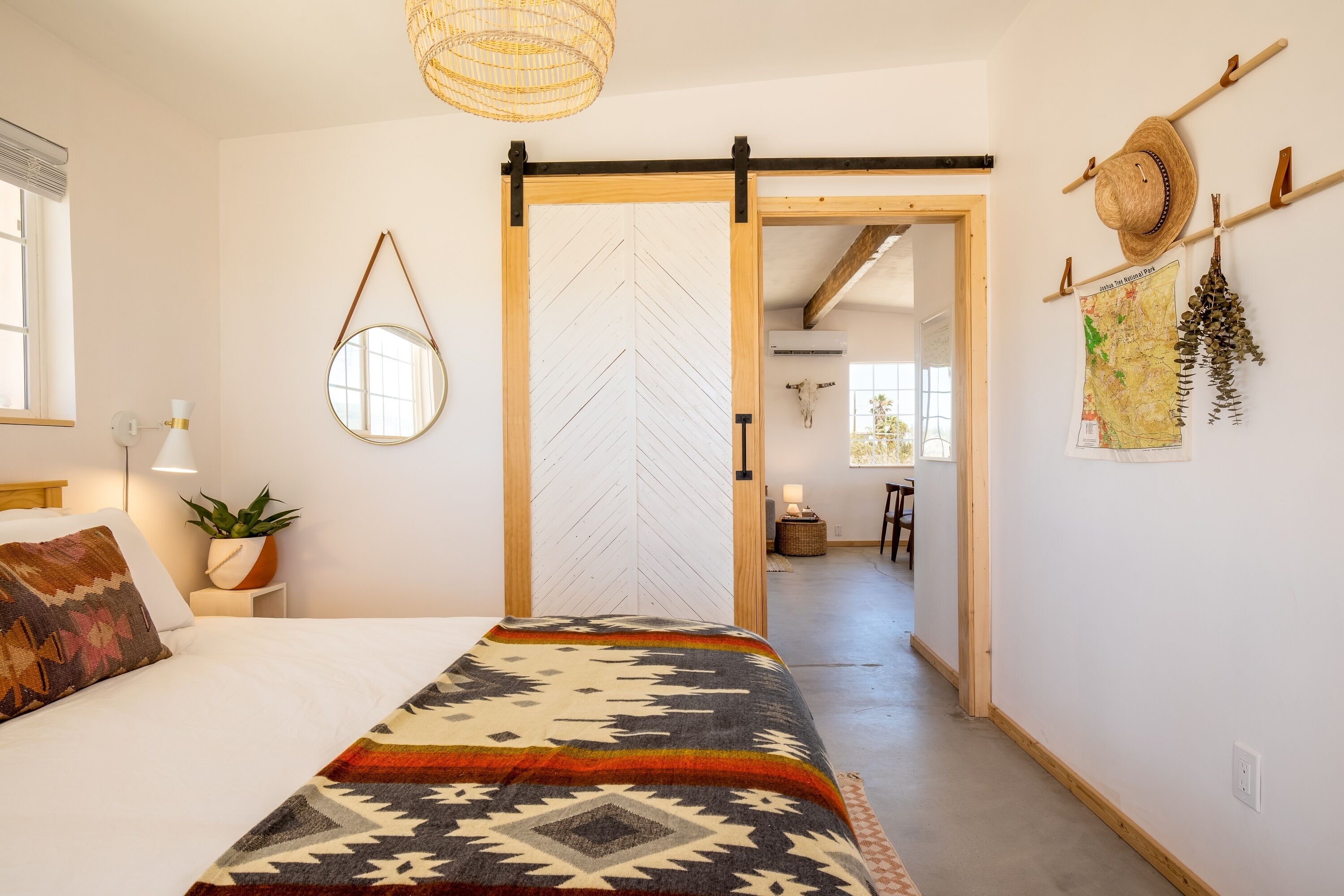 Een slaapkamer met een bed, een spiegel aan de muur, een potplant, een hoedrek en een schuifdeur naar een andere kamer.