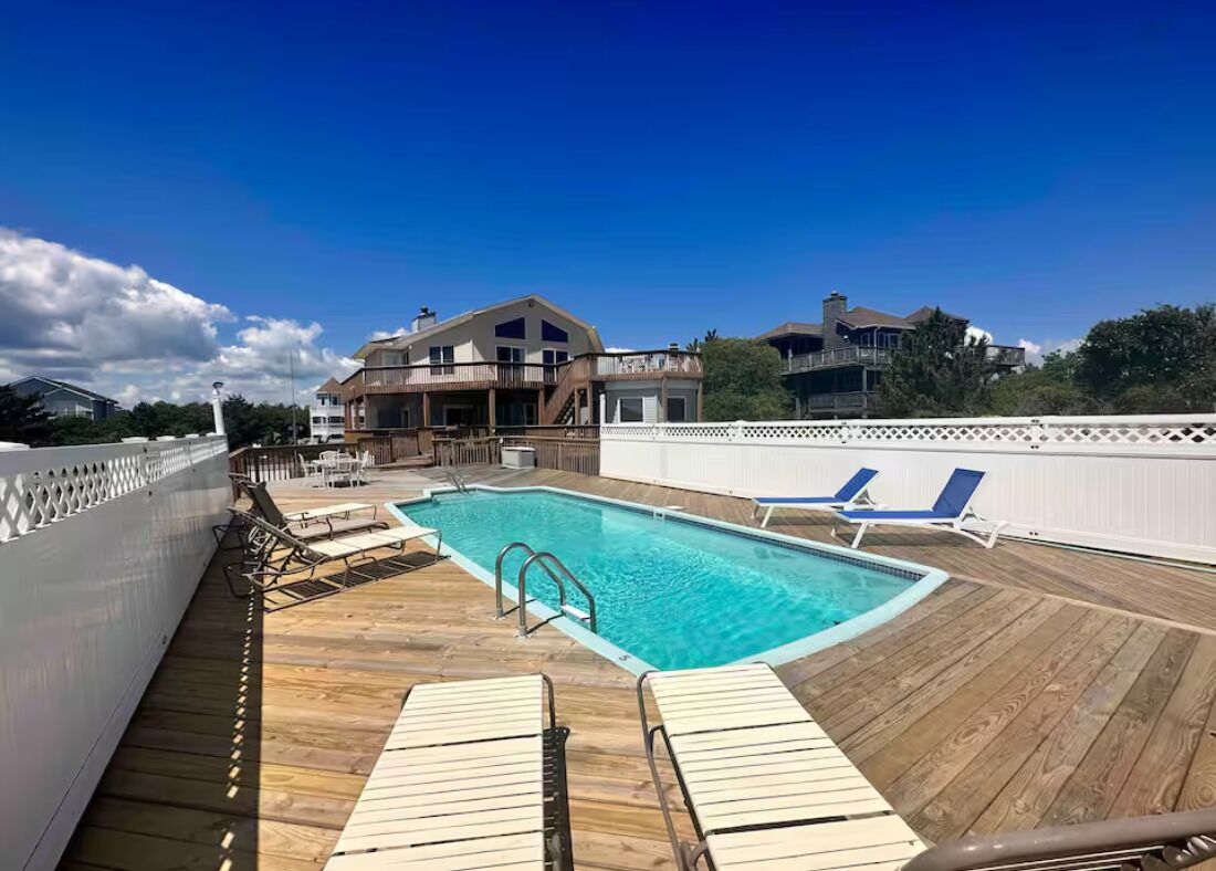 Eine Holzterrasse mit Swimmingpool, Liegestühlen und einem weißen Zaun.