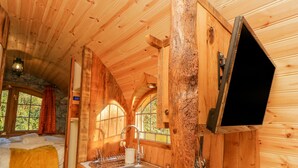 A wooden cabin interior with a bed, a sink, and a window.
