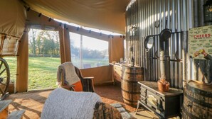 A rustic tent interior with a large window, a wooden stove, and a metal wall with a sign.