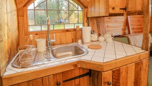A wooden cabin kitchen with a large window, a sink, and basic kitchen amenities.