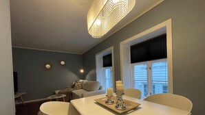 A dining area with a white table set for four, a chandelier, and a window with blinds. - Charming 2-bed Apartment in Stavanger (Stavanger)