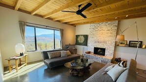 Uma sala de estar ampla, com uma janela grande, lareira e ventilador de teto.