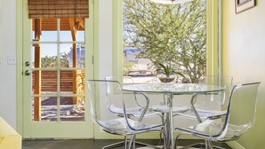 A dining area with a glass table and chairs, a hanging light fixture, and a view of a tree through a window. - Martian Rose - Out Of This World Stargazing Cabin 2 Bedroom Home by RedAwning (Joshua Tree)