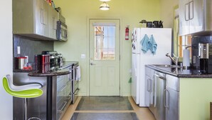A compact kitchen with stainless steel appliances, a green door, and a small seating area with a green chair. - Martian Rose - Out Of This World Stargazing Cabin 2 Bedroom Home by RedAwning (Joshua Tree)